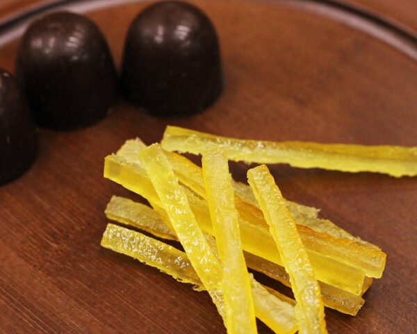Our candied lemon peels come from a top producer in France with over 100 years of history. Our suppliers employ traditional production methods to expertly remove bitterness and soften the peels. They gently cook the lemon strips in a sweet syrup, allowing them to absorb the fragrant lemon goodness. The intense aroma of lemon with a refreshing sour flavor brings out another side of the chocolate.